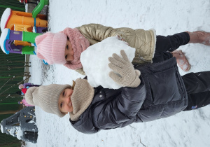 Dwie dziewczynki trzymają w rękach bryłę śniegu.