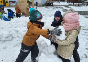 Dzieci podają sobie śniegowe kule.