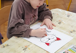 Dziewczynka koloruje rysunek konturowy kota.