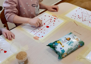 Dziewczynka wykonuje eksperyment z kropkami farby na foli.