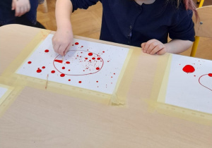 Dziewczynka wykonuje eksperyment z kropkami farby na foli.