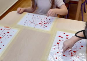 Dziewczynka wykonuje eksperyment z kropkami farby na foli.