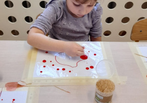 Dziewczynka wykonuje eksperyment z kropkami farby na foli.