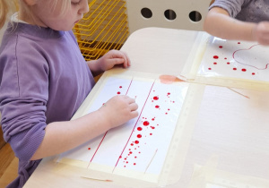 Dziewczynka wykonuje eksperyment z kropkami farby na foli.