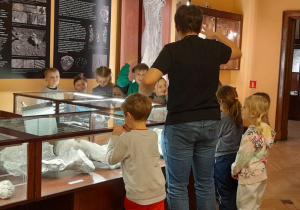 Dzieci oglądają eksponaty umieszczone w gablotach.