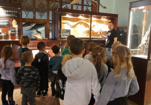 Dzieci oglądają eksponaty umieszczone w gablotach.