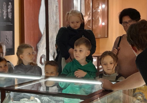 Dzieci oglądają eksponaty umieszczone w gablotach.