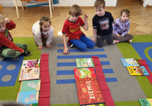 Dzieci układają na przygotowanych "półkach" z krepiny książki. Zadaniem jest ułożenie ich po 7 na półce - wprowadzenie cyfry 7.