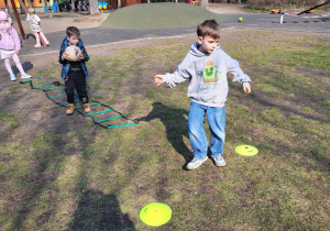 Dwaj chłopcy wykonują slalom z piłką i strzał na bramkę.