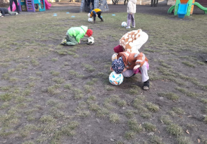 Dzieci turlają piłkę głową.