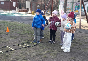 Dzieci wykonują sportowy tor przeszkód z piłką.