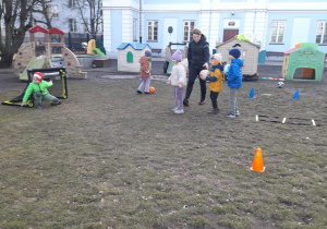 Dzieci wykonują sportowy tor przeszkód z piłką.