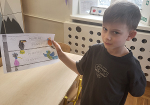 Chłopiec prezentuje wykonaną przez siebie kartę pracy.