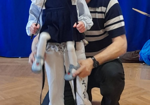 Dziewczynka uczy się posługiwać lalką teatralną podczas warsztatów teatralnych.