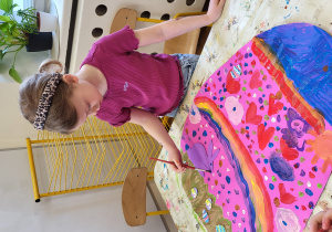 Dziewczynka maluje duże jajo z brystolu.