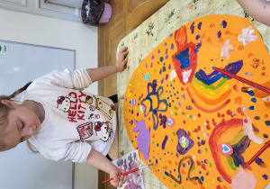 Dziewczynka maluje duże jajo z brystolu.