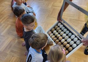 Dzieci siedzą na podłodze i oglądają rożnego koloru jajka zniesione przez kury.