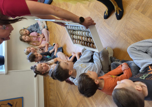 Dzieci siedzą na podłodze i oglądają rożnego koloru jajka zniesione przez kury.