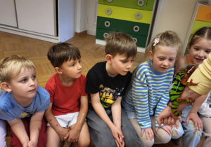Dzieci oglądają kameleona siedzącego na ręce opiekunki.